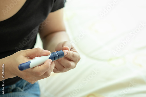 Woman using lancet on finger to check blood sugar level by Glucose meter on bed in the morning . Medicine, diabetes, glycemia, health care and people concept.