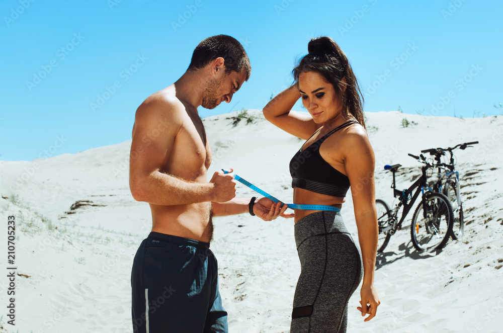 two athletes, a boy and a girl, play sports on the beach. guy black girl Asian . training of cyclists . the guy measures the waist of a girl two athletes, a boy and a girl, play sports on the beach. guy black girl Asian . training of cyclists . the guy measures the waist of a girl