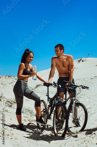 two athletes, a boy and a girl, play sports on the beach. guy black girl Asian . cyclists resting. drink water
