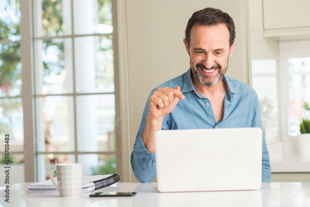 Middle age man using laptop at home pointing with hand and finger up with happy face smiling Middle age man using laptop at home pointing with hand and finger up with happy face smiling