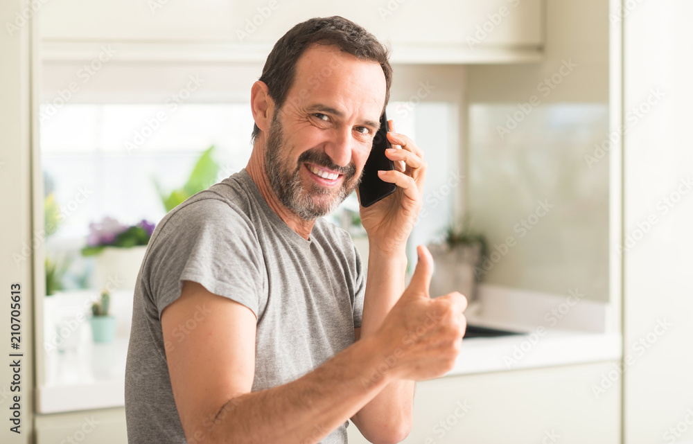 Middle age man using smartphone happy with big smile doing ok sign, thumb up with fingers, excellent sign Middle age man using smartphone happy with big smile doing ok sign, thumb up with fingers, excellent sign