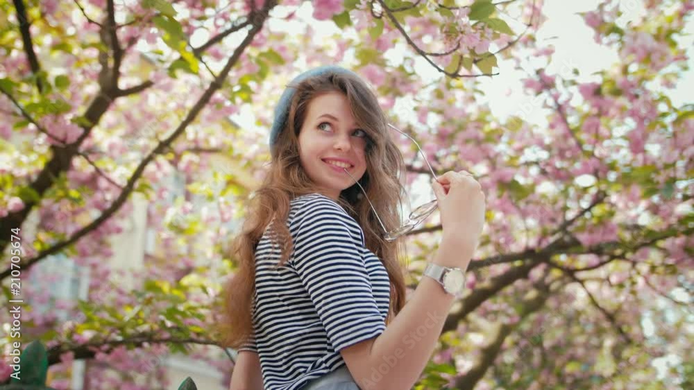 Young beautiful happy smiling lady wearing beret and striped shirt posing under the blooming sakura Young beautiful happy smiling lady wearing beret and striped shirt posing under the blooming sakura