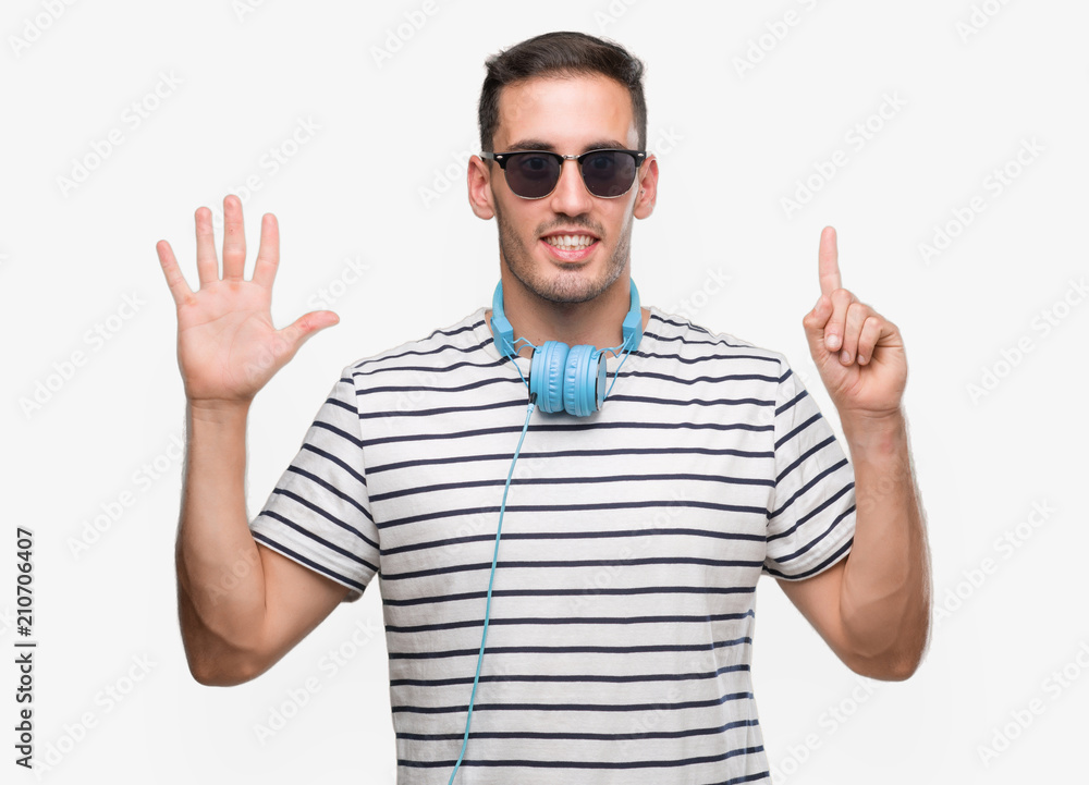 Handsome young man wearing headphones showing and pointing up with fingers number six while smiling confident and happy. Handsome young man wearing headphones showing and pointing up with fingers number six while smiling confident and happy.