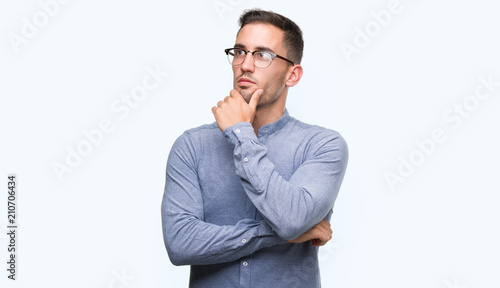 Handsome young elegant man wearing glasses looking confident at the camera with smile with crossed arms and hand raised on chin. Thinking positive.