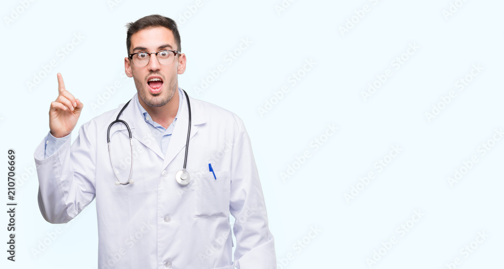 Handsome young doctor man pointing finger up with successful idea. Exited and happy. Number one. Handsome young doctor man pointing finger up with successful idea. Exited and happy. Number one.