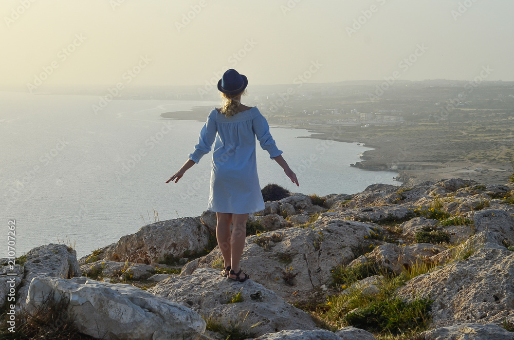 Tourist woman standing on mountain and looking on sea. Wanderlust travel concept, space for text, atmospheric epic moment. Cape Greco, Cyprus, Mediterranean Sea
