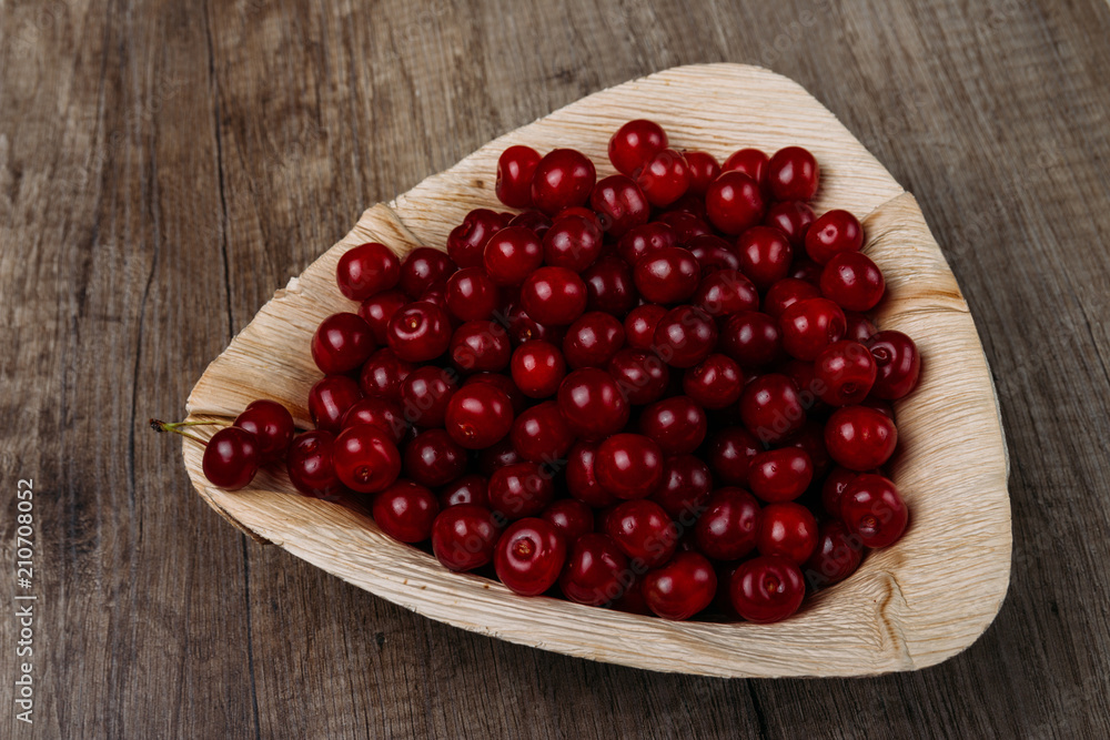 fresh red cherries in a wooden plate on a wooden table. wooden plate on a wooden background. a plate in the form of a triangle. ecology. proper nutrition. fresh red cherries in a wooden plate on a wooden table. wooden plate on a wooden background. a plate in the form of a triangle. ecology. proper nutrition.
