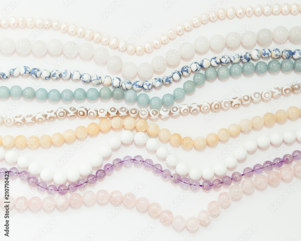 Set of threads different semiprecious gemstones beads in light pastel colors,pink quartz,white agate,pearls,jade,violet amethyst,greenstone and turquoise on the white background,top flat lay view. Set of threads different semiprecious gemstones beads in light pastel colors,pink quartz,white agate,pearls,jade,violet amethyst,greenstone and turquoise on the white background,top flat lay view.