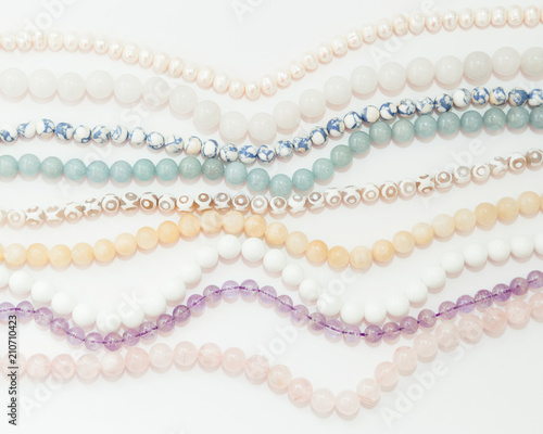 Set of threads different semiprecious gemstones beads in light pastel colors,pink quartz,white agate,pearls,jade,violet amethyst,greenstone and turquoise on the white background,top flat lay view.