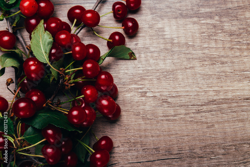 summer gifts. a fresh branch of a cherry tree with green leaves and red fruits, cherries lying on a wooden table, on a wooden background. Protect the environment. proper nutrition.place for text photo