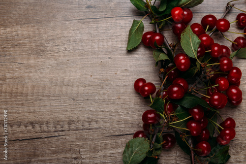 summer gifts. a fresh branch of a cherry tree with green leaves and red fruits, cherries lying on a wooden table, on a wooden background. Protect the environment. proper nutrition.place for text