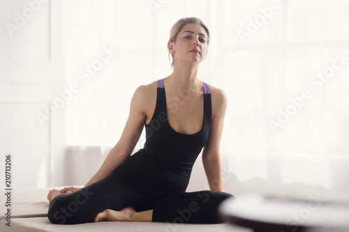 Relaxed attractive woman practicing yoga on mat near window