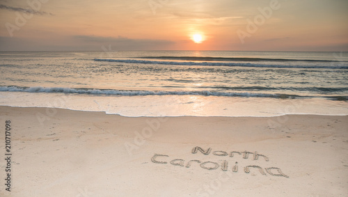 The words North Carolina etched in the sand at sunrise with waves coming ashore.