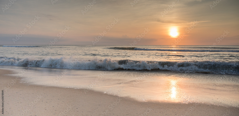 The sun rising over the ocean at sunrise with waves crashing ashore.