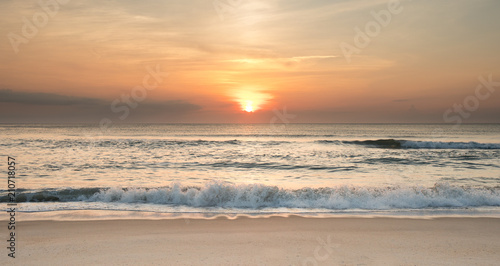 The sun rising over the ocean at sunrise with waves crashing ashore.