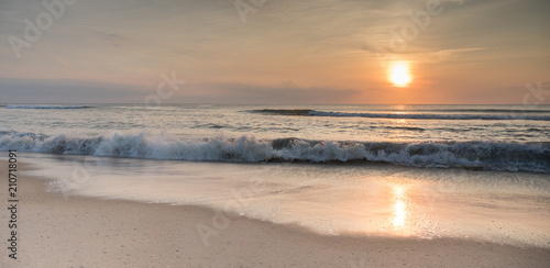 The sun rising over the ocean at sunrise with waves crashing ashore.