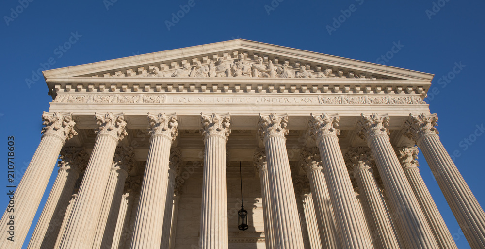 Looking up at the US Supreme Court building in Washington, DC with a bright blue sky.