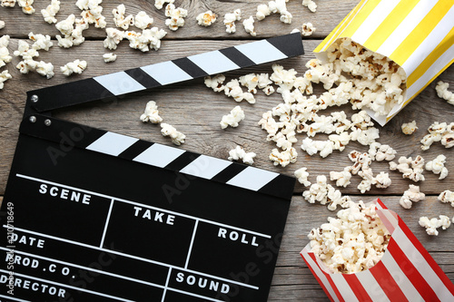 Clapper board with popcorn in paper bags on wooden table
