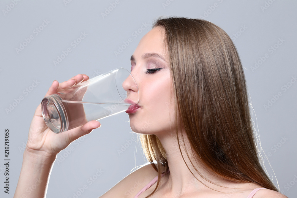 Young woman drinking water on grey background Young woman drinking water on grey background