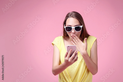 Portrait of young woman in sunglasses with smartphone on pink background © 5second