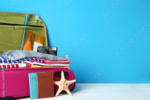 Opened suitcase with clothes, camera and sunscreen bottles on wooden table