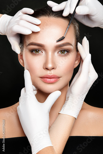 Beautiful woman portrait with classical make up and hands in medical gloves with cosmetic tool.