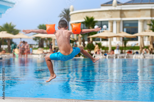 Obraz na płótnie Caucasian boy having fun making fantastic jump into swimming pool at resort. His arms and legs are wide open. w salonie