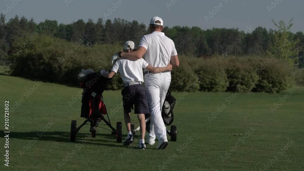 Happy man with his son golfers walking on perfect golf course at summer day Happy man with his son golfers walking on perfect golf course at summer day