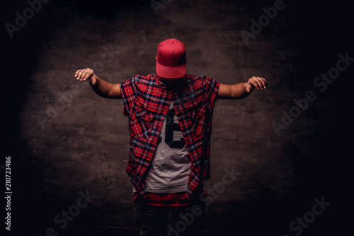 Portrait of an African-American dancer guy dressed in a red fleece shirt and cap at the studio. Isolated on dark textured background. photo