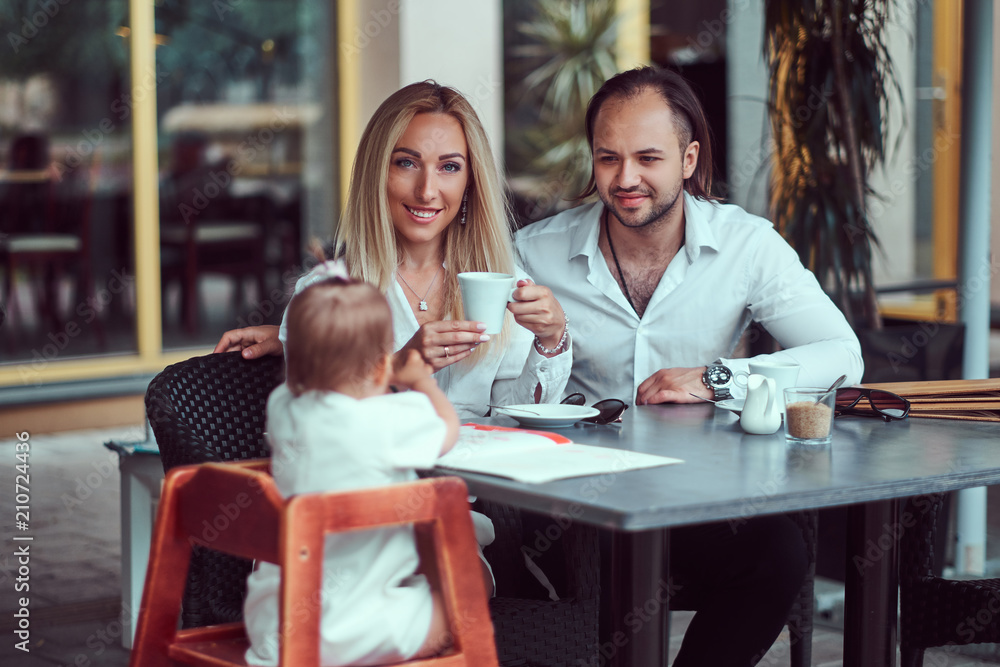 Family and people concept - happy mother, father and the little girl in outdoor cafe.