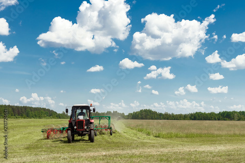 Agricultural machinery  a tractor collecting grass in a field against a blue sky. Hay harvesting  grass harvesting. Season harvesting  grass  agricultural land.