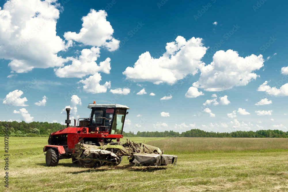 Agricultural machinery, harvester mowing grass in a field against a blue sky. Hay harvesting, grass harvesting. Season harvesting, grass, agricultural land. Agricultural machinery, harvester mowing grass in a field against a blue sky. Hay harvesting, grass harvesting. Season harvesting, grass, agricultural land.