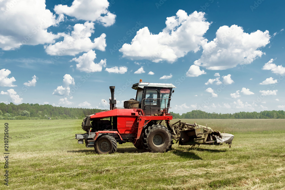 Agricultural machinery, harvester mowing grass in a field against a blue sky. Hay harvesting, grass harvesting. Season harvesting, grass, agricultural land. Agricultural machinery, harvester mowing grass in a field against a blue sky. Hay harvesting, grass harvesting. Season harvesting, grass, agricultural land.