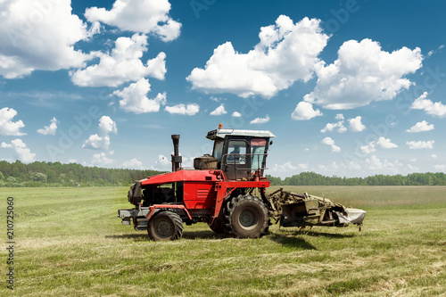 Agricultural machinery, harvester mowing grass in a field against a blue sky. Hay harvesting, grass harvesting. Season harvesting, grass, agricultural land.