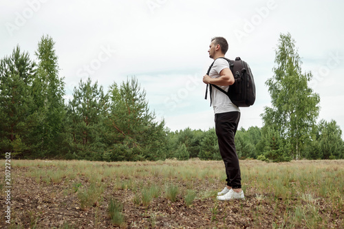 Portrait of a young man, a wanderer with a backpack. Goes on the road with a copy space, a happy tourist on a summer day, a traveler enjoying his time relaxing in nature.