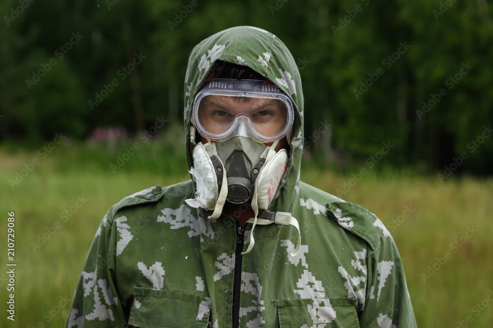 A man in a respirator and glasses and a camouflage suit against the background of nature. Chemical armies.