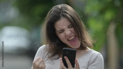Young happy beautiful woman looking excited while using phone in the streets outdoors
