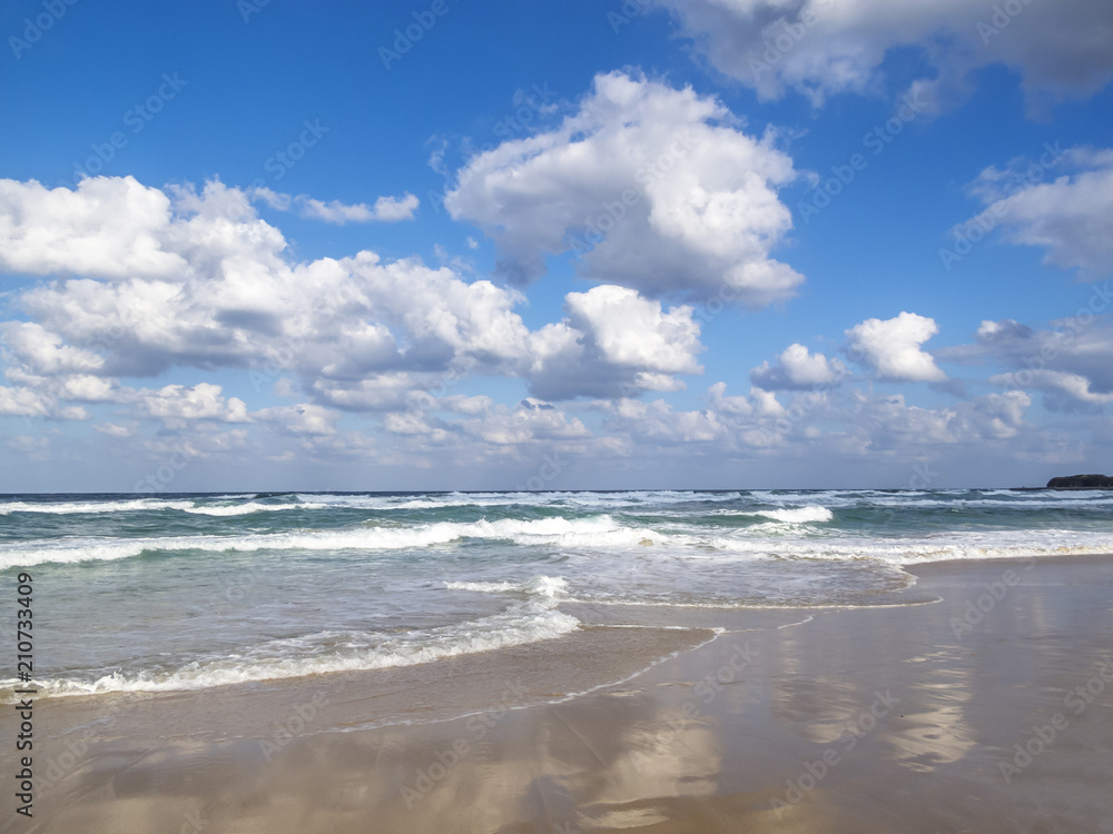 Waves spreading on a sandy Black Sea beach, cloud reflections on the sand, cumulus clouds in the sky