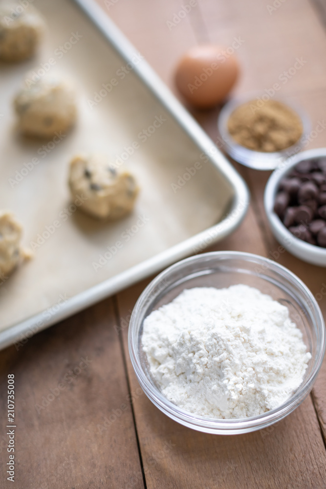 Close up on a bowl of flour with chocolate chip cookie baking scene in the blurry background Close up on a bowl of flour with chocolate chip cookie baking scene in the blurry background