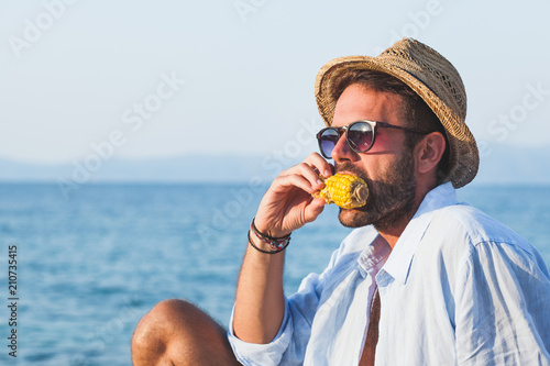Young man eating corn on the beach