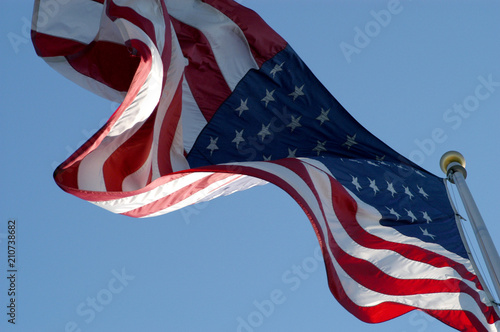 Looking up at United States Flag waving in the breeze. American flag on a flag pole waving in the wind against a blue sky, no clouds, no people. Looking up at US flag on a sunny day.