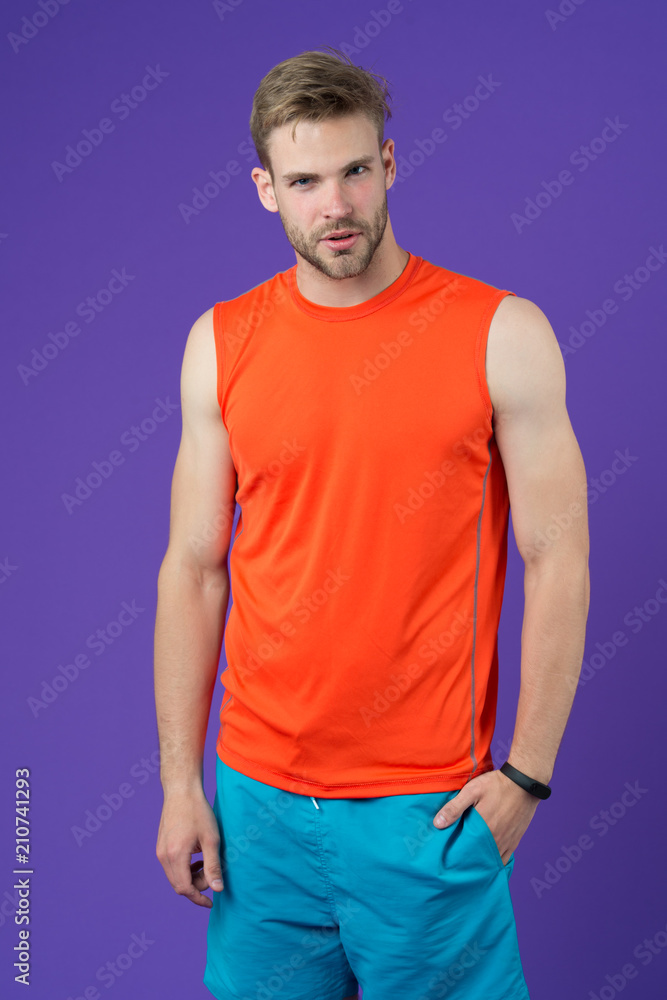 Athlete on violet background. Muscular man in orange vest and blue shorts, sportswear fashion. Fit and confident. Sport fashion for training and workout. Fitness and wellness Athlete on violet background. Muscular man in orange vest and blue shorts, sportswear fashion. Fit and confident. Sport fashion for training and workout. Fitness and wellness