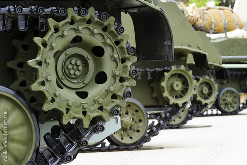 Tank tracks and steel wheels of heavy armored vehicles with green bodywork in row, military industry, modern army equipment, selective focus 
