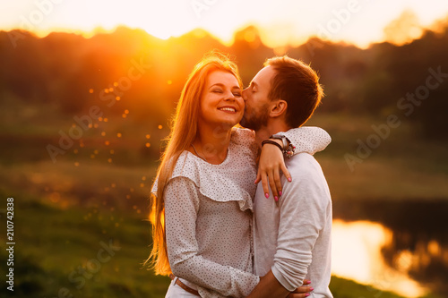 A guy with a beard gently kisses his girlfriend on a cheek and s