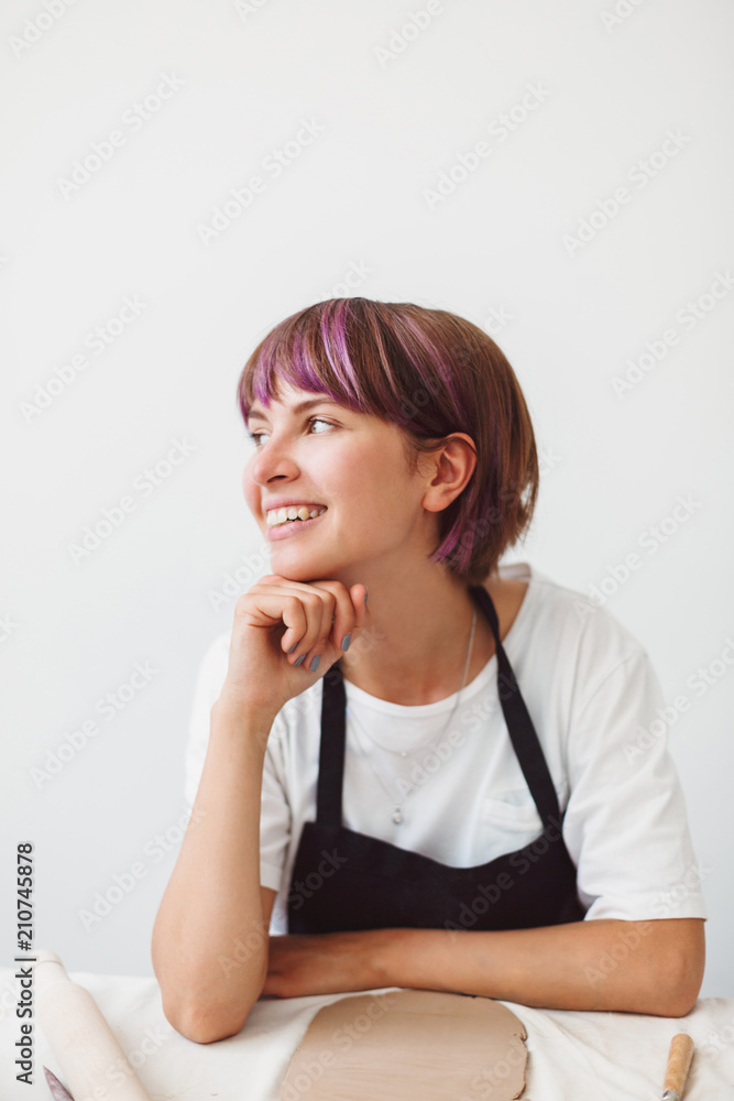 Beautiful smiling girl with colorful hair in white T-shirt dreamily looking aside happily spending time at pottery studio Beautiful smiling girl with colorful hair in white T-shirt dreamily looking aside happily spending time at pottery studio