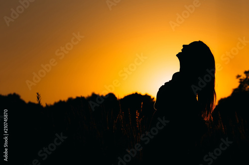 silhouette of a girl who sincerely laughs against the background of the evening sky among the high grass