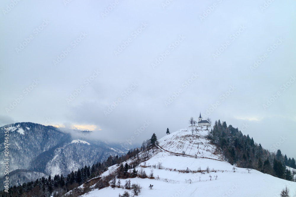 Small church on a snowy hill in the middle of a mountain range