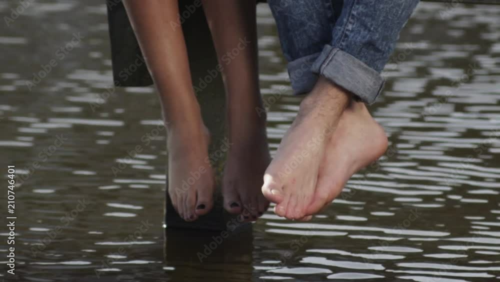 Close up, couple hangs feet over lake Close up, couple hangs feet over lake