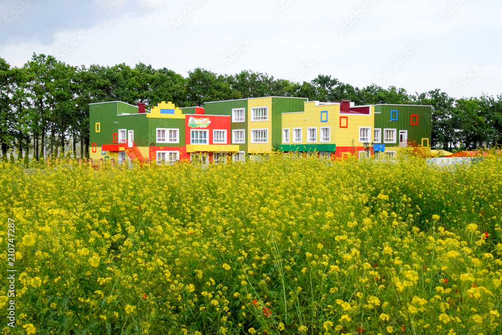 The building of a kindergarten behind a clearing of yellow flowers. The building of a kindergarten behind a clearing of yellow flowers.