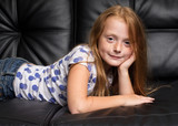Little redhead girl with freckles resting on black sofa